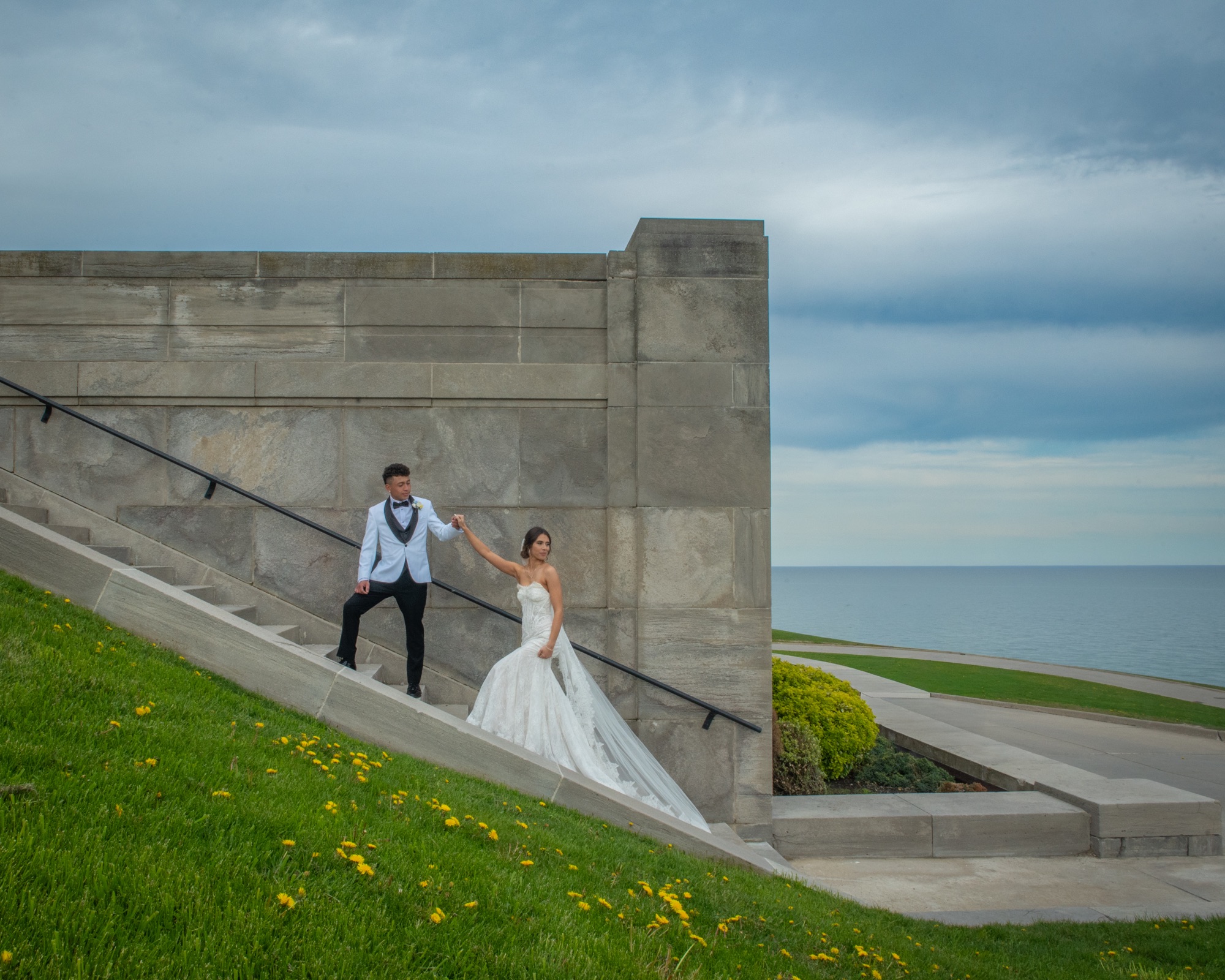 A newly married couple holding hands on architectural stone steps by the lake